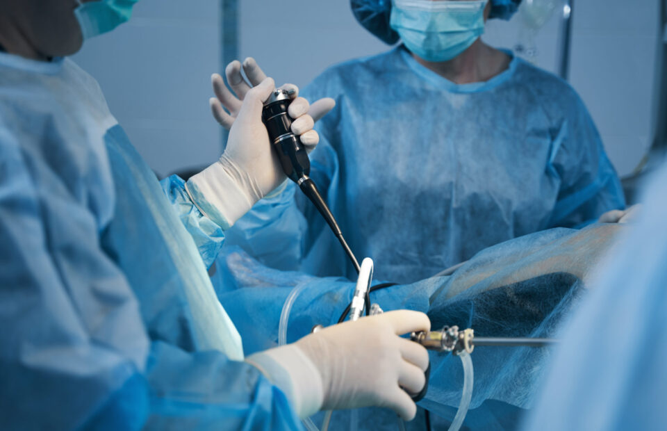 Cropped photo of two doctors in surgical gowns standing near the patient and using hysteroscope